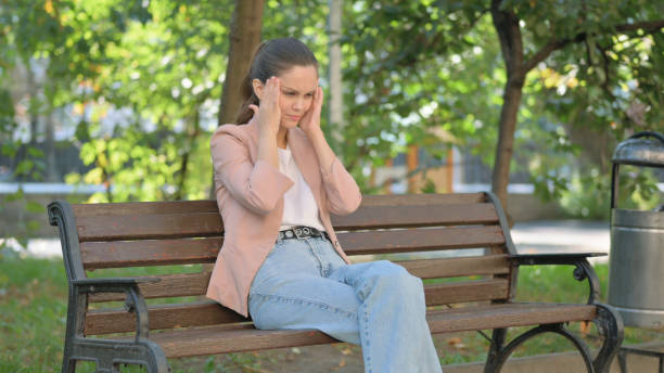 istock Young Woman with Headache Sitting in Park 2194609192
