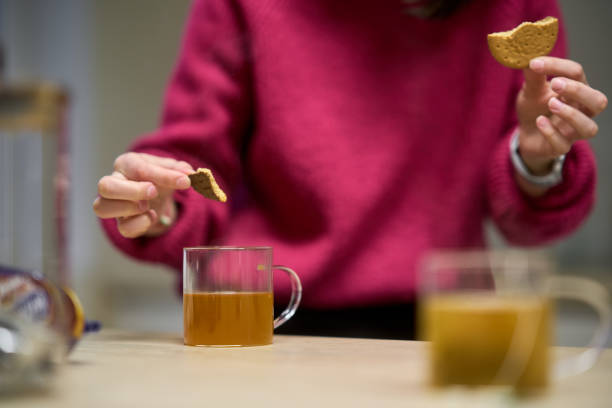 Young woman dunking a digestive biscuit in a glass cup of herbal tea, enjoying a relaxing moment at home