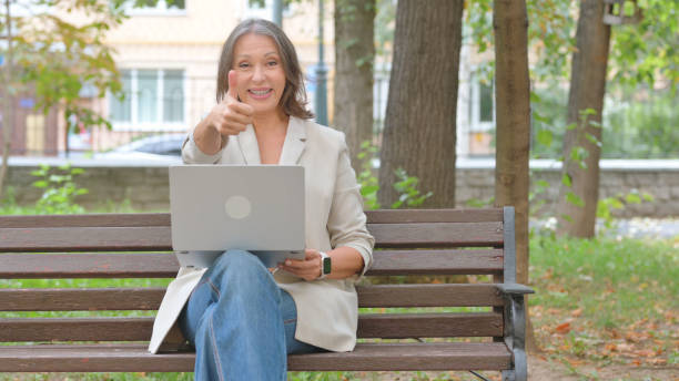 istock Thumbs Up by Old Senior Woman Using Laptop in Park 2194612320