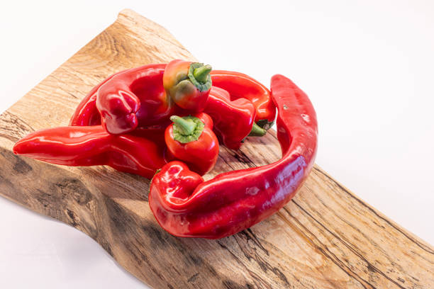 Bent, wonky, ugly looking red pointed peppers that supermarkets may refuse due to their unusual shape. satin a wooden cutting board Isolated on a white background