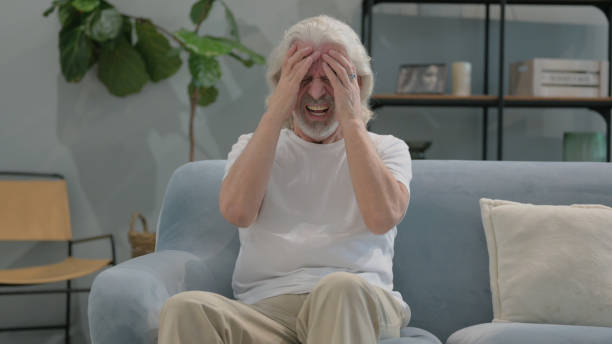 istock Old Man with Headache Sitting on Sofa at Home 2194617975