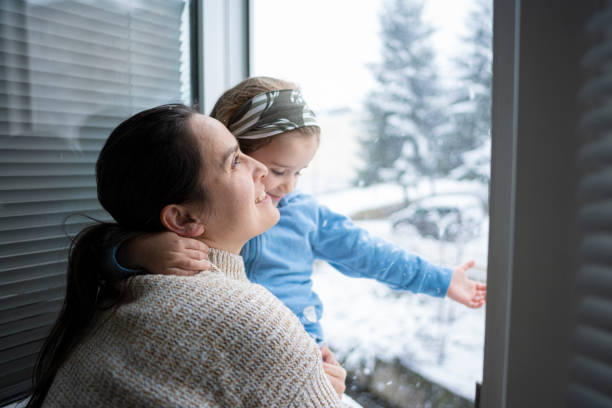 istock Happy Mom & Child Looking Through Window At Winter Snowfall 2194618167
