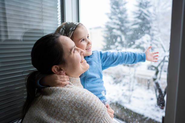 Happy Child in Mom's Hands Touching Snowflakes from Window