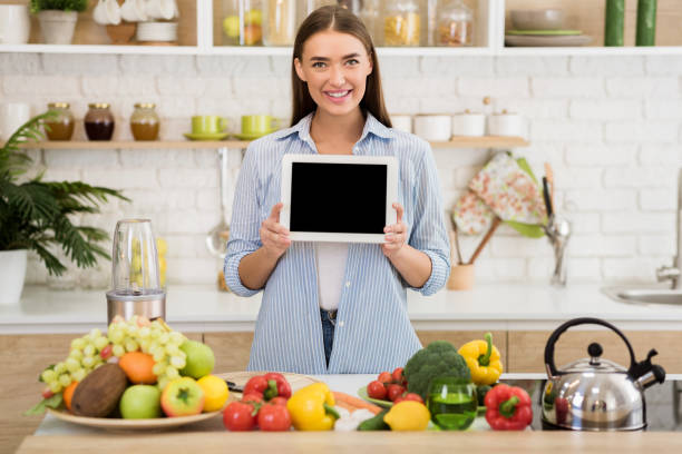 istock Young Woman Holding Tablet While Surrounded by Fresh Fruits and Vegetables in a Bright Kitchen 2194623514
