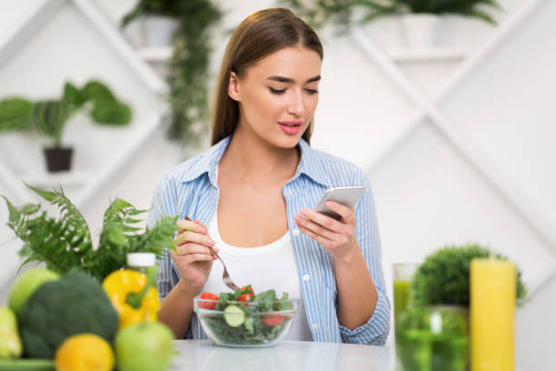 istock Woman Enjoying a Healthy Salad While Using Her Smartphone in a Bright Kitchen 2194623543