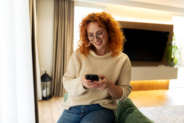 istock Beautiful young female sitting on a couch and sending message using her smart phone 2194624394
