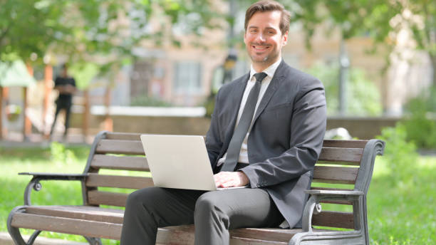 istock Middle Aged Businessman Smiling at Camera while Using Laptop Outdoor 2194624466