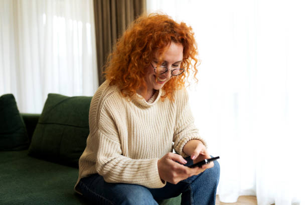 istock Beautiful young female sitting on a couch and sending message using her smart phone 2194624575
