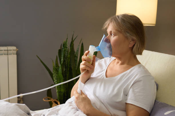 istock A woman sits in bed using a nebulizer, addressing her respiratory condition. She appears focused and calm, highlighting the importance of home care in managing health 2194629292