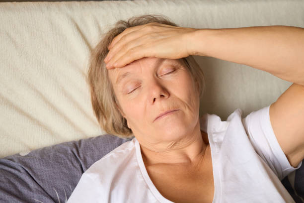 istock A middle-aged woman lies in bed, eyes closed and forehead pressed with one hand, reflecting discomfort. Soft lighting fills a cozy bedroom, indicating daytime 2194629310