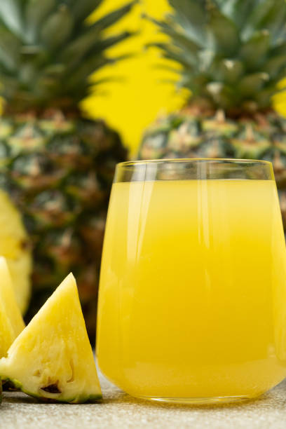 Pineapple juice in a glass among fresh pineapple fruit close-up