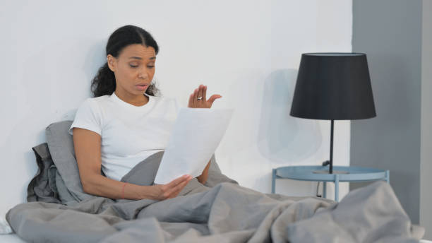 istock Tense African Woman Shocked while Reading Report in Bed 2194633791