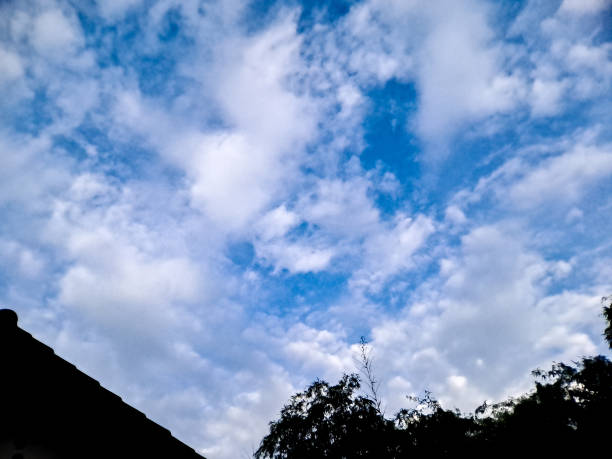 istock Dramatic silhouette of rooftops and a tree against a vibrant blue sky with fluffy clouds. Perfect for urban landscape photography 2194634342