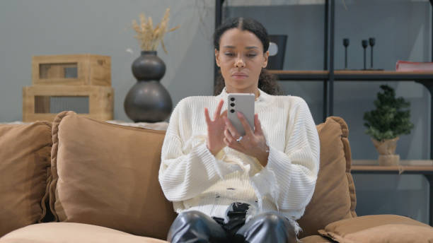 istock African Woman Browsing Internet on Phone at Home 2194635999