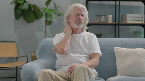 istock Old Man with Neck Pain Sitting on Sofa at Home 2194636209