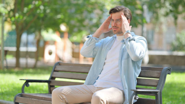 istock Casual Young Man with Migraine Sitting in Park 2194636429