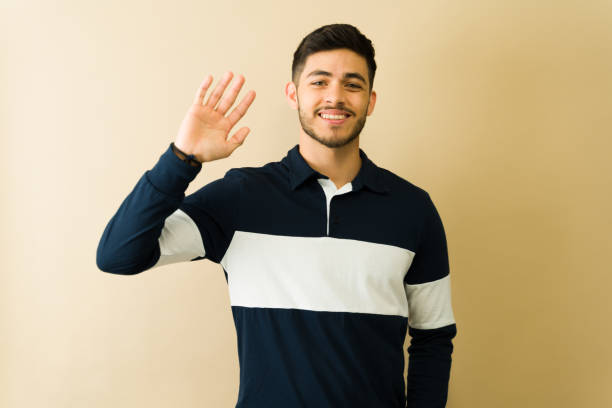 istock Hispanic young man waving hand and smiling on beige background 2194639165