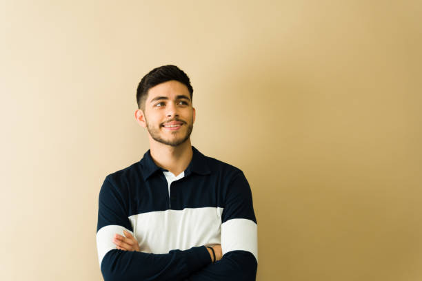 istock Young man smiling and looking up with crossed arms on beige background 2194639257