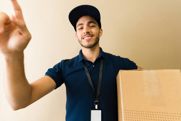 istock Smiling delivery man pressing the doorbell button while holding cardboard box 2194639481