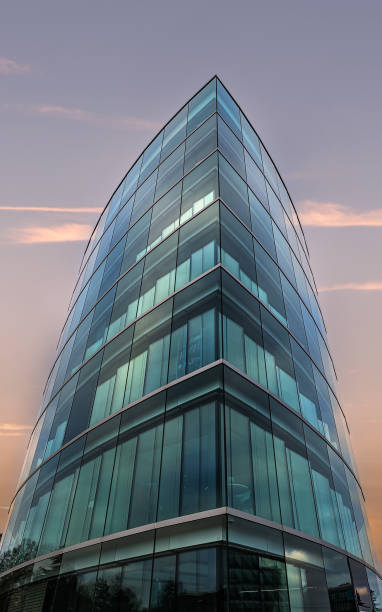 Modern skyscraper captured from a low angle, showing a curved facade with a grid of reflective glass windows and metal framing, emphasizing the building’s height, symmetry, and contemporary architectural design.