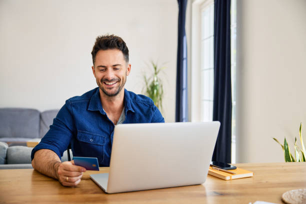 istock Smiling man at home shopping online paying with credit card using laptop 2194654412