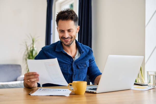 istock Smiling man looking at financial document working remote on laptop 2194654562
