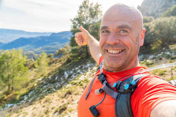 istock Smiling hiker taking a selfie while pointing at mountain peak 2194659007