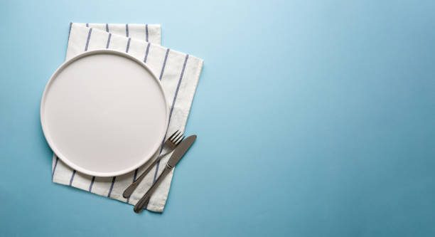 istock Top view of empty ceramic white plate and cutlery on blue background 2194659278