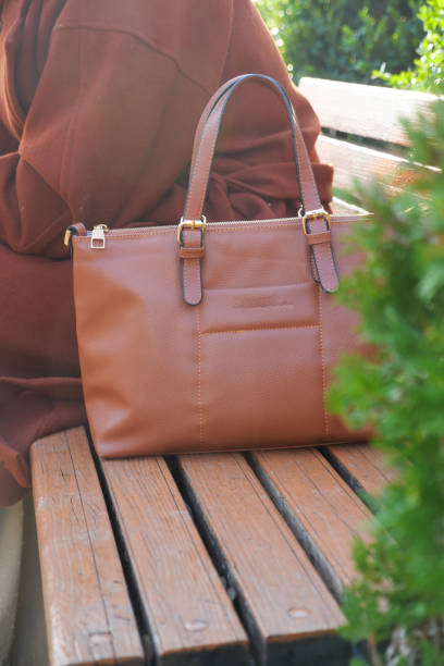 A stylish brown handbag is beautifully placed on a bench in a serene outdoor setting