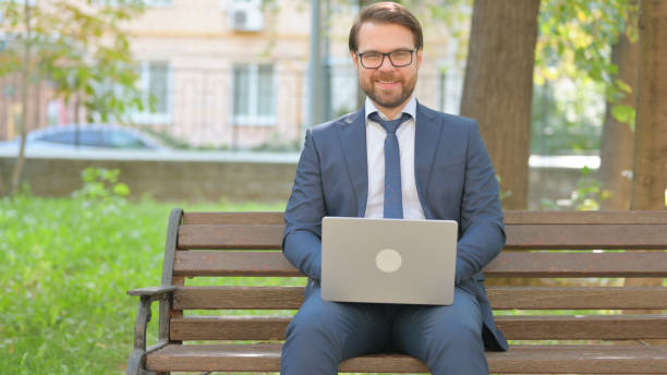 istock Businessman in Glasses Smiling at Camera while Using Laptop Outdoor 2194670725