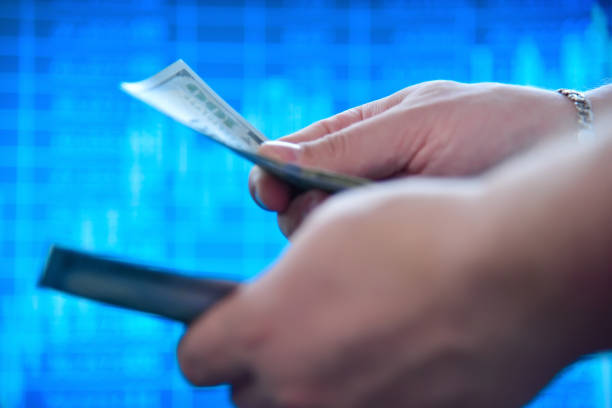 Hands counting dollar bills. Finance and investments concept. Close upHands holding and counting us dollar bills. Finance and investments concept. Close upHand extends a large wad of american dollars to another hand against the background of business charts on the screen