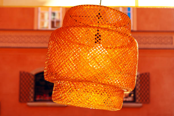 An intricate orange hanging lamp with a layered design takes center stage. The blurred backdrop showcases a building's windows and decorative details, enhancing the scene's aesthetic charm
