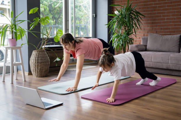 istock Mother and little daughter doing home exercises watching online tutorial 2194679359