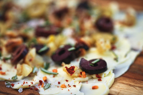 A beautifully styled butter board featuring a spread of creamy butter, garnished with green and black olives, fresh herbs, and spices