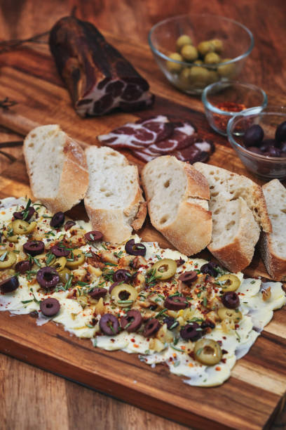 Rustic Butter Board with Olives, Herbs, and Garnishes on Wooden Surface