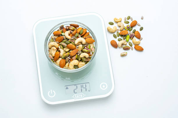 istock Healthy eating: overhead view of assorted nuts and seeds portion on a kitchen scale isolated on white background 2194688695