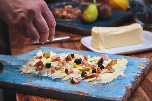 Preparing Butter Board with Fresh Figs, Blueberries, and Honey Drizzle on a Rustic Blue Background