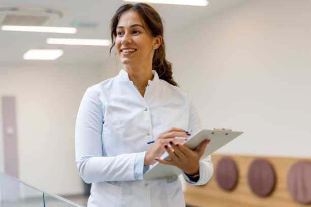Young female doctor writing notes on clipboard in hospital corridor