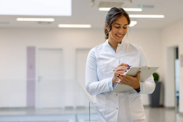 istock Young female doctor writing notes on clipboard in hospital corridor 2194689735