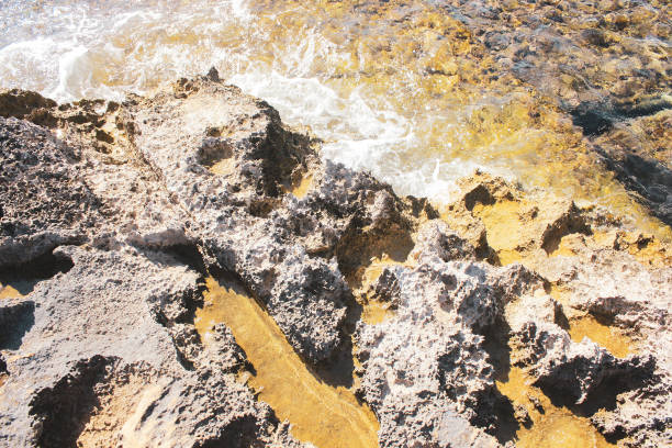 Rocky beach, consisting largely of sandstone formations, at the small fishing village of Agia Ermioni at the eastern coastline of the Greek Island of Chios in the Aegean Sea on a sunny morning in autumn (October). The image was captured on old-fashioned 35mm daylight ISO 200 film by an analogue (or analog) 35 mm film camera. The granularity in the image is real film grain (due to the presence of small particles of dyed silver halide on the negative). Minimal post processing has been done (only adjustment of histogram). The image is part of a series of rocky beaches on the Greek Island of Chios.