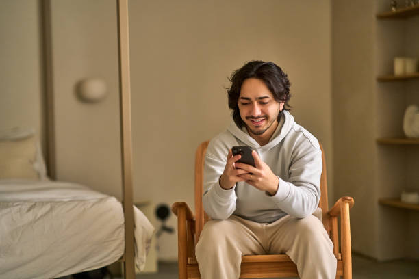 istock Young man sitting on rocking chair using smartphone at home 2194698448