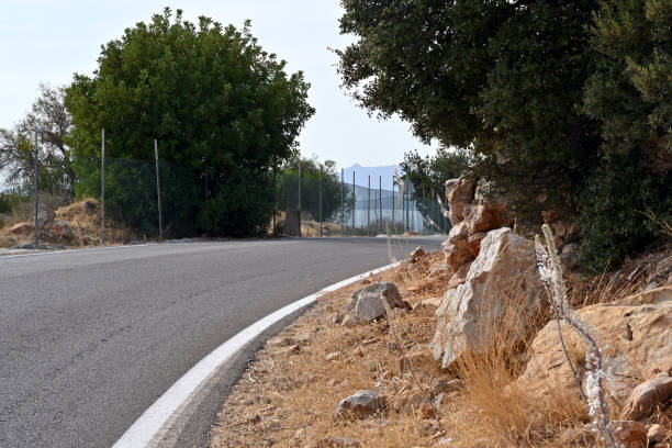 istock A downhill asphalt road bordered by bushes and stones. 2194705920