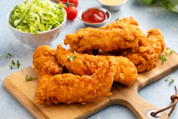 istock Fried chicken tenders on a serving board with sauces and salad 2194717791