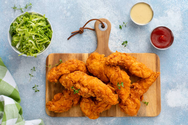 istock Fried chicken tenders on a serving board with sauces and salad 2194717801