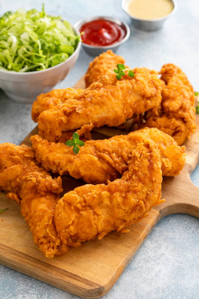 istock Fried chicken tenders on a serving board with sauces and salad 2194717803
