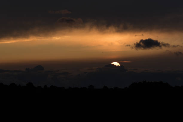 Sunset time, sun almost hiding behind some big cloud on the horizon, yellowish dramatic sky, backlit hill on the foreground