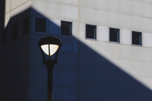 Isolated streetlamp against modern architecture with dramatic shadow play. Minimalist composition highlighting geometric shapes and contrasting light.
