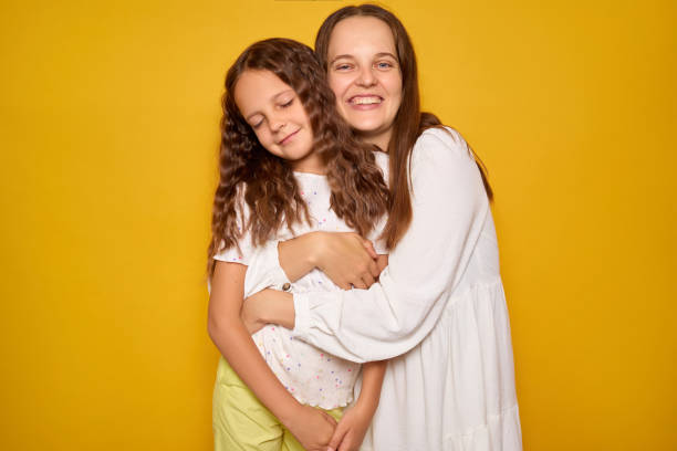 istock Two girls express affection with a warm hug, both smiling widely. One has long, curly hair while the other enjoys a playful pose in a bright, cheerful setting 2194721317