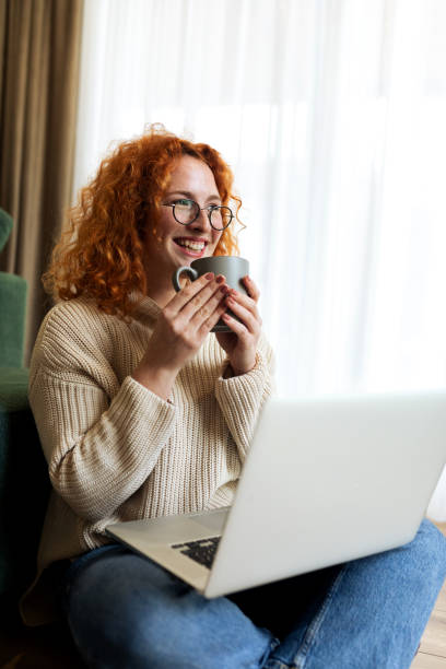 istock Young woman sitting on the floor in her living room while using laptop computer and drinking coffee 2194724723