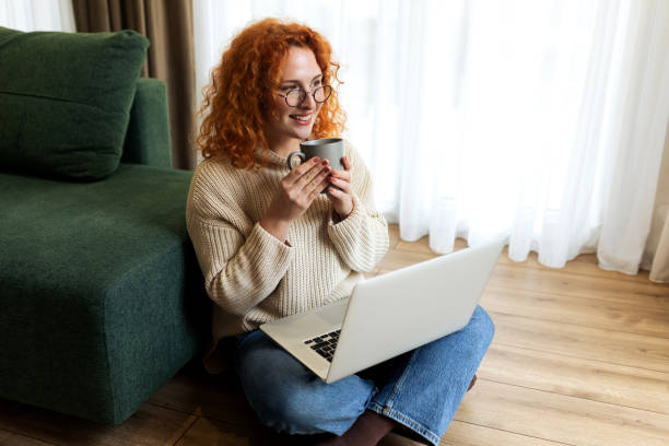 istock Young woman sitting on the floor in her living room while using laptop computer and drinking coffee 2194724724